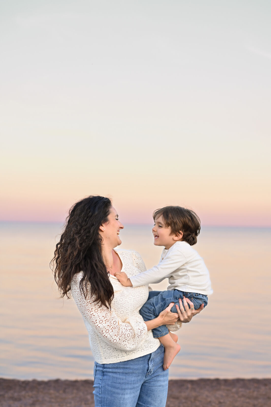 Mamma che solleva il figlio ridendo sulla spiaggia al tramonto