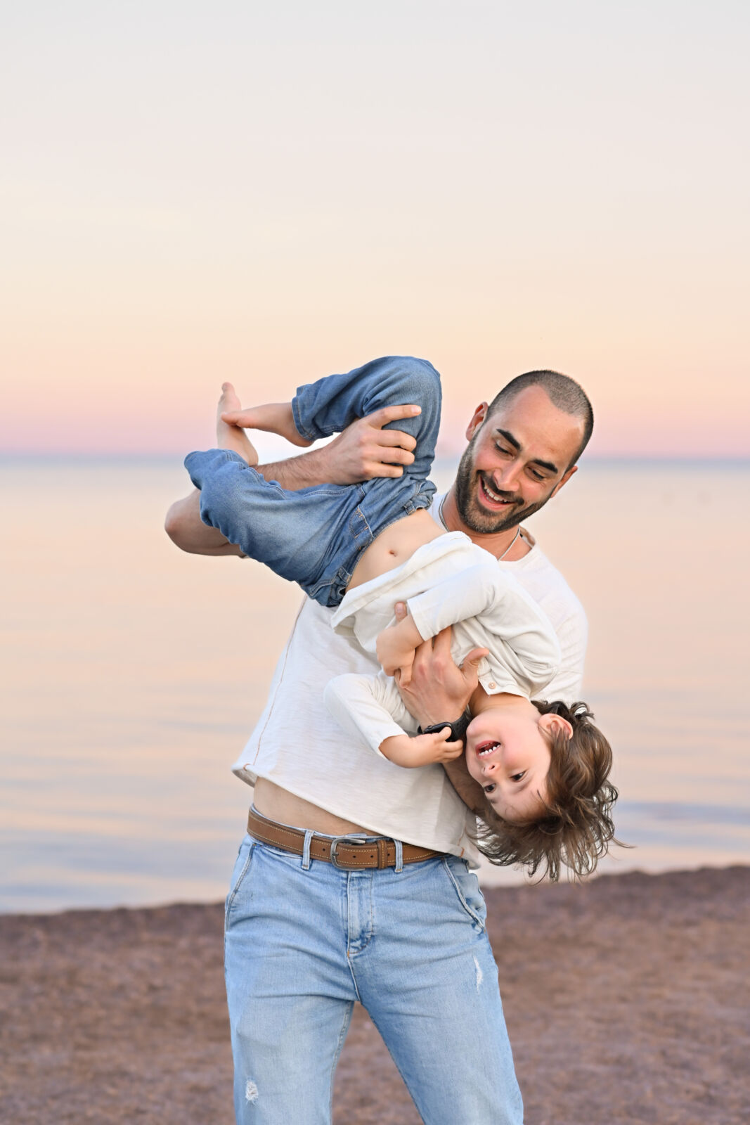Papa' che tiene i due figli a testa in giu' sulla riva del mare