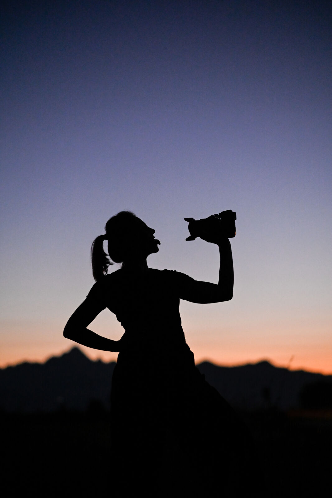 Silhouette di una fotografa che scatta contro il cielo rosso del tramonto