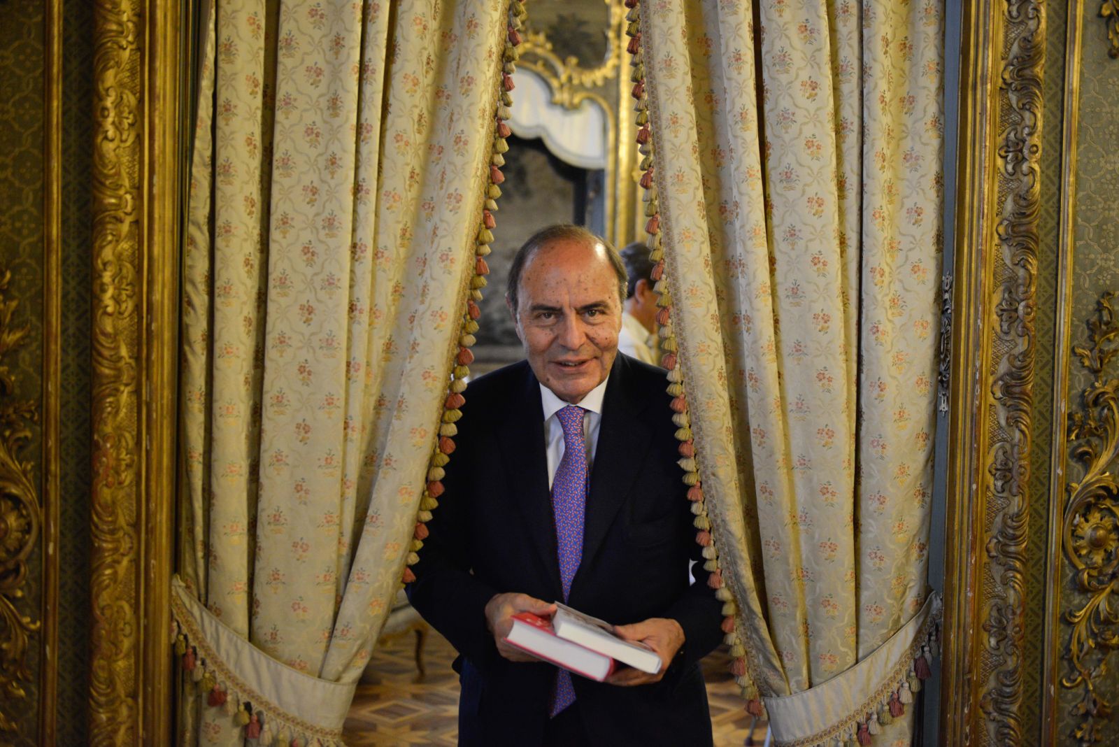 Il celebrante legge la formula di rito davanti a tende damascate dorate