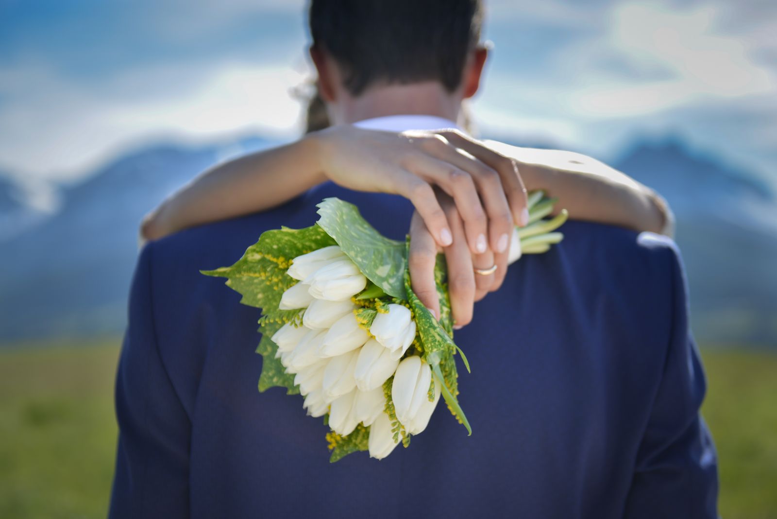 Bouquet di tulipani bianchi tra le mani della sposa che abbraccia lo sposo