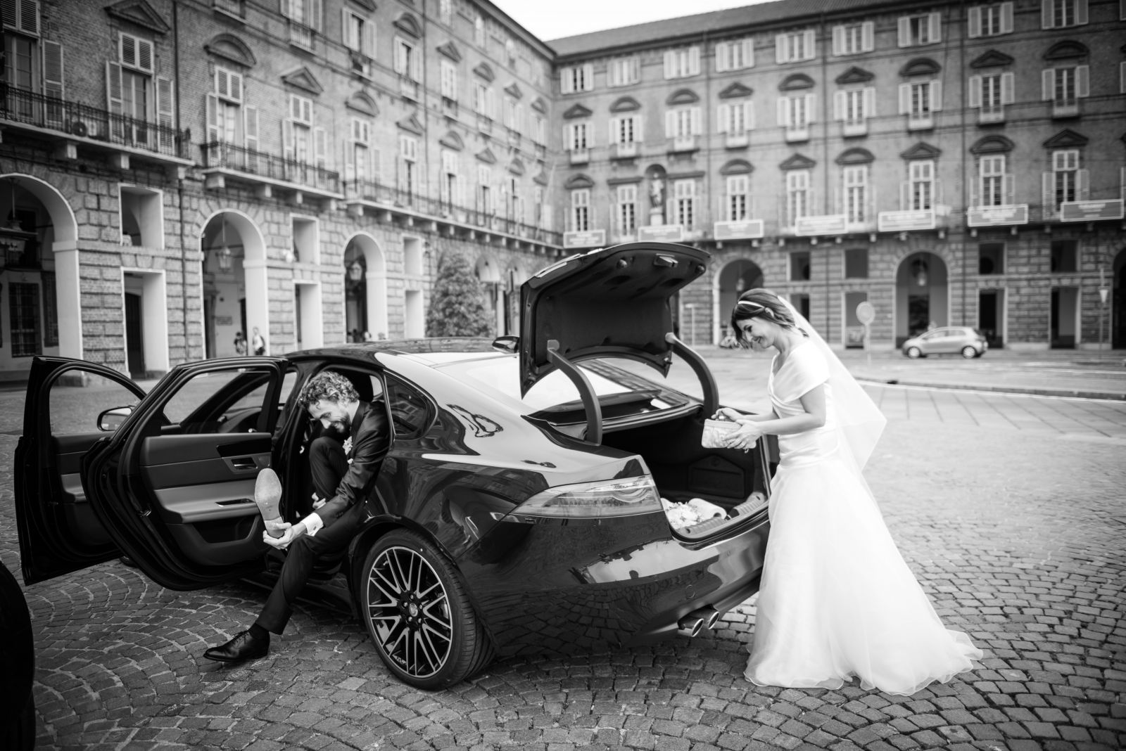 Sposa che scende dall'auto in una piazza storica, fotografia in bianco e nero