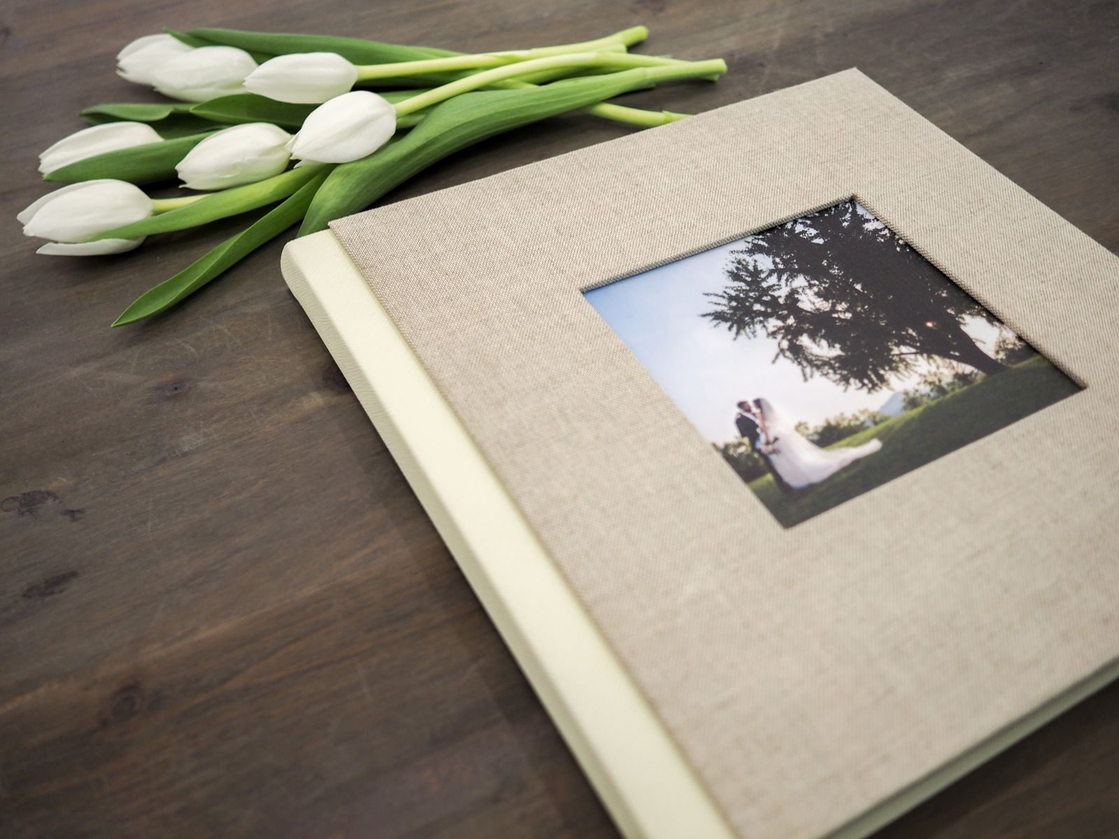 Fotolibro in lino con finestra fotografica in copertina accanto a tulipani bianchi
