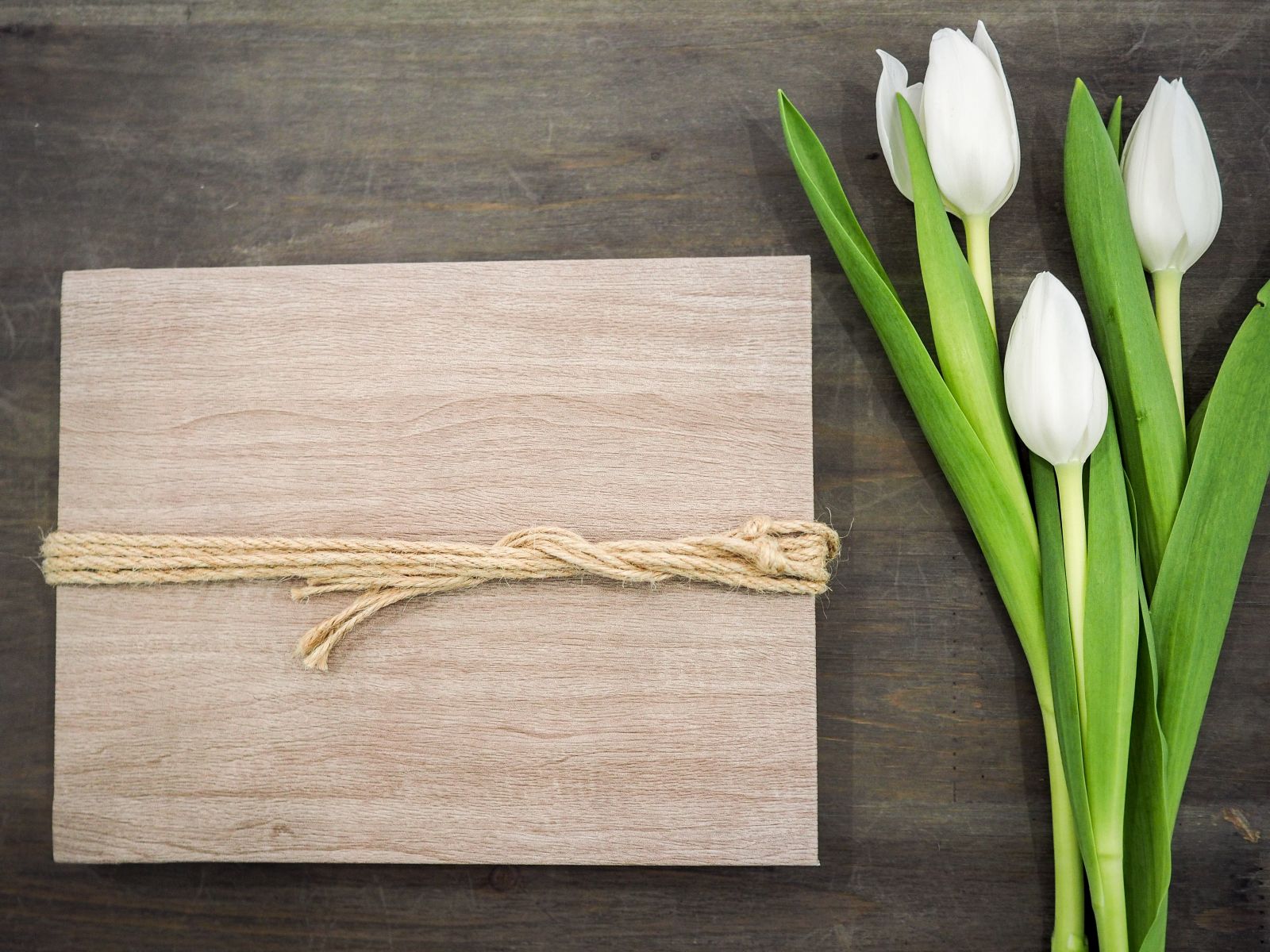 Copertina in legno legata con spago accanto a un mazzo di tulipani bianchi